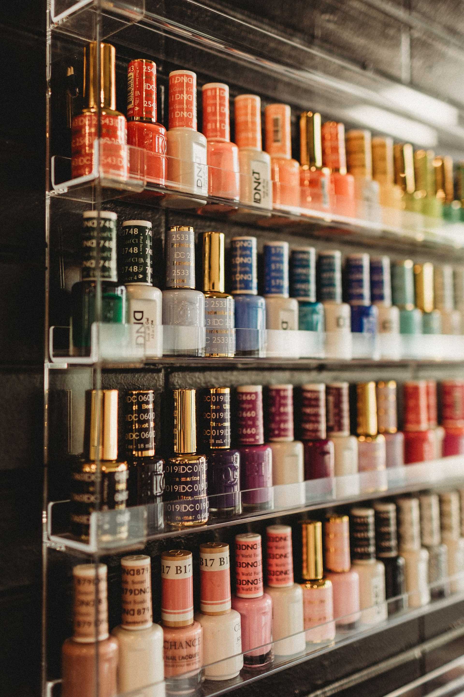 Nail polish bottles in various colors neatly arranged on clear shelves in a salon.