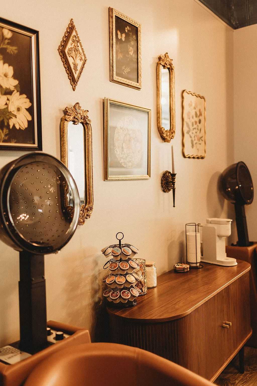 Vintage salon interior with ornate mirrors, art frames, and coffee station on a wooden counter.