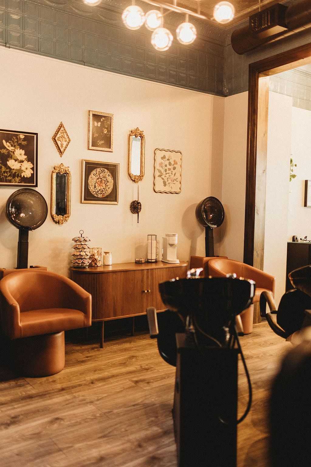 Chic vintage salon with stylish chairs, wall art, and old-fashioned hair dryers.