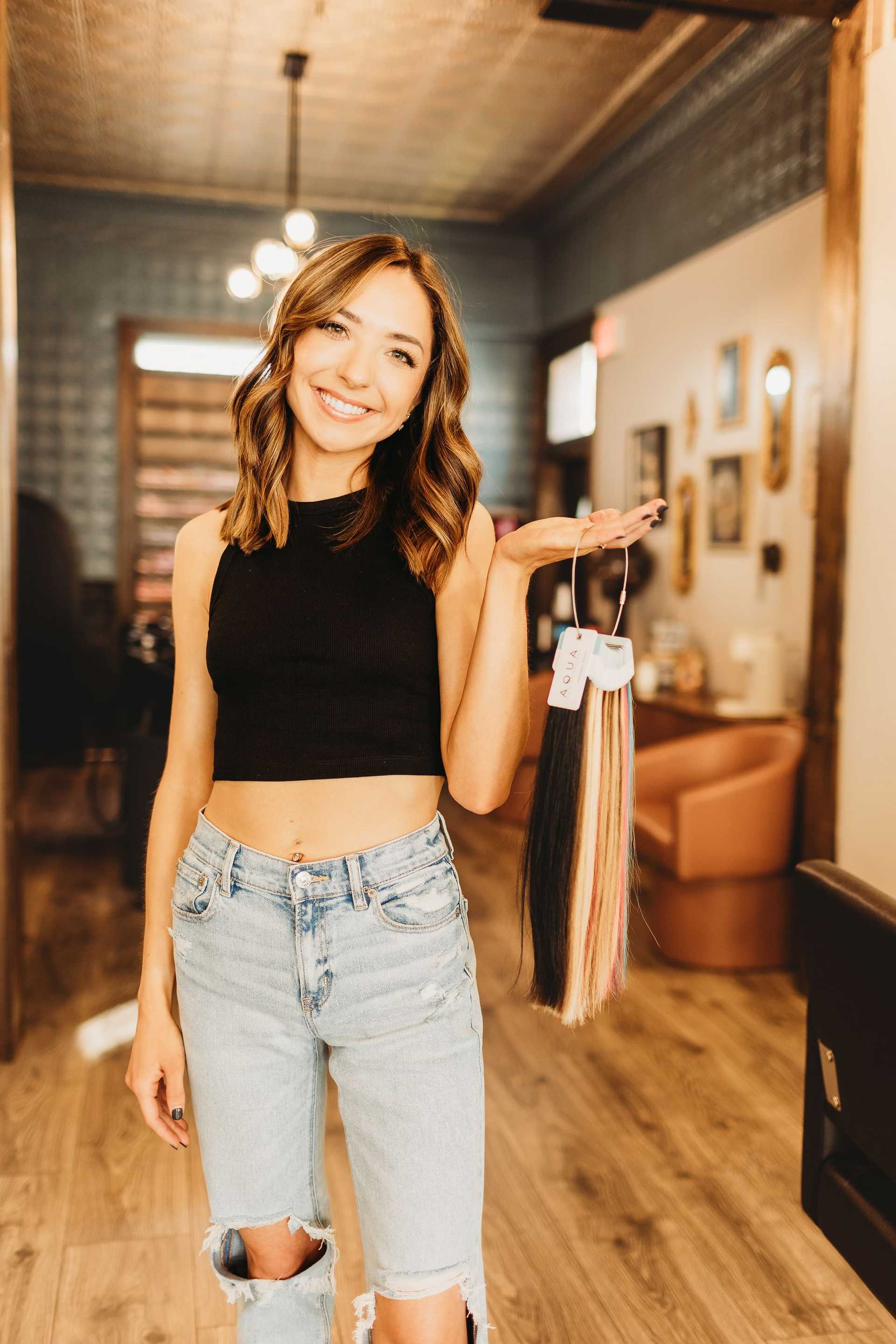 Young woman in salon, holding hair color samples, smiling confidently.
