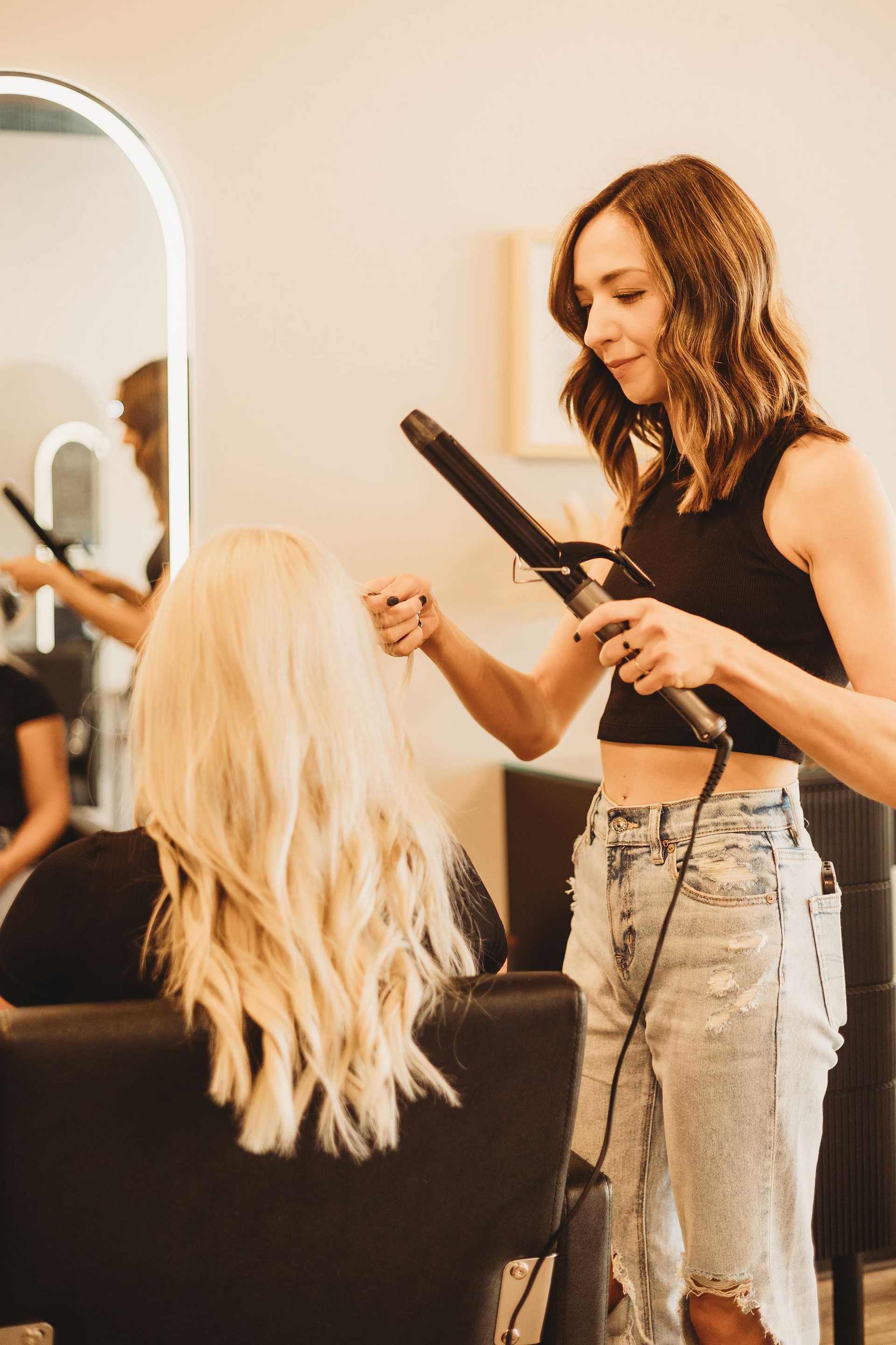Stylist curling a client's long blonde hair in a salon.